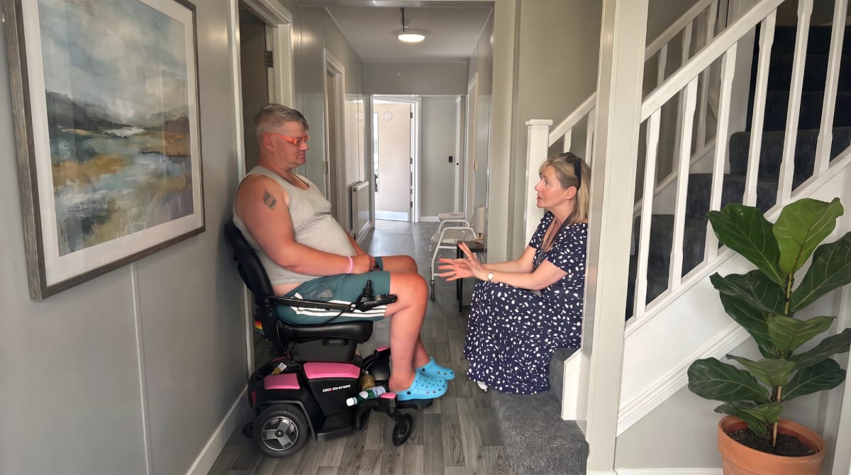Woman sitting on the stairs talking with a man in a powered wheelchair in a hallway